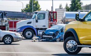 A semi-truck sits in the foreground of the picture at a traffic light next to a totaled blue car.
